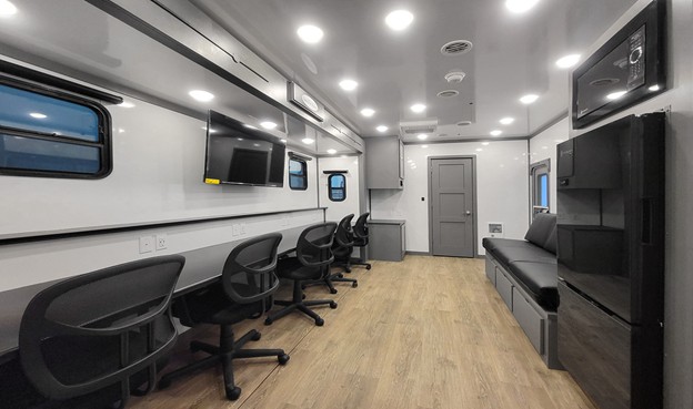 Interior of a modern command center with multiple black chairs, two wall TVs, and a black sofa bench.